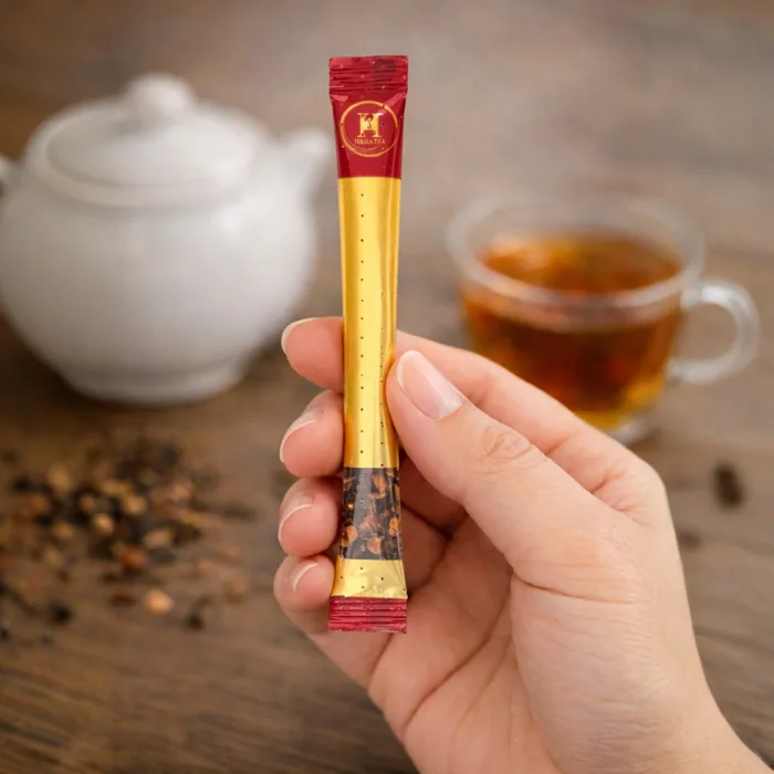 Kézben tartott stick tea, háttérben teáskanna és csésze