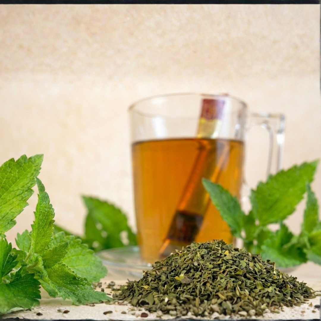Pure Mint stick tea makró: friss mentalevél és aprított menta, háttérben tea üvegcsészében stickkel.